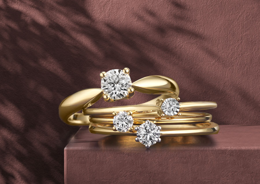 Elegante goldene Verlobungsringe und Solitärringe mit funkelnden Diamanten in verschiedenen Größen auf warmem braunem Hintergrund mit Schattenwurf